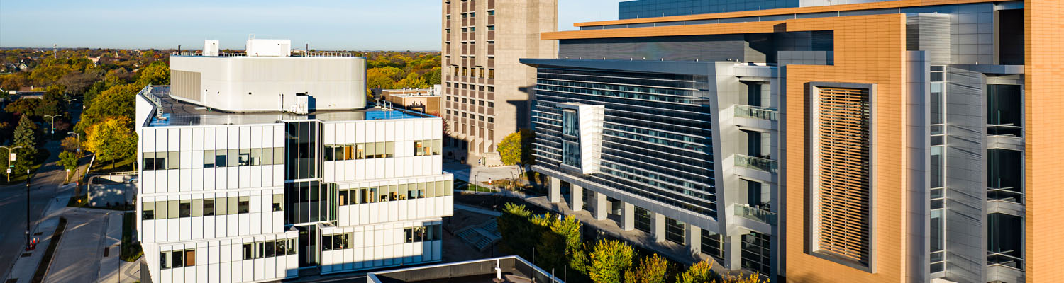 Aerial view of UWM campus buildings with mixed architectural styles surrounded by green spaces and residential areas.