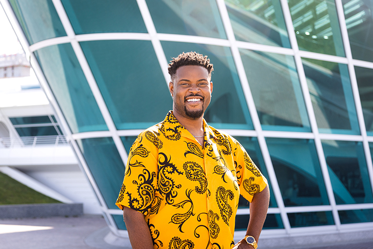 Black male UWM student wearing a yellow shirt and standing in front of the Milwaukee Art Museum