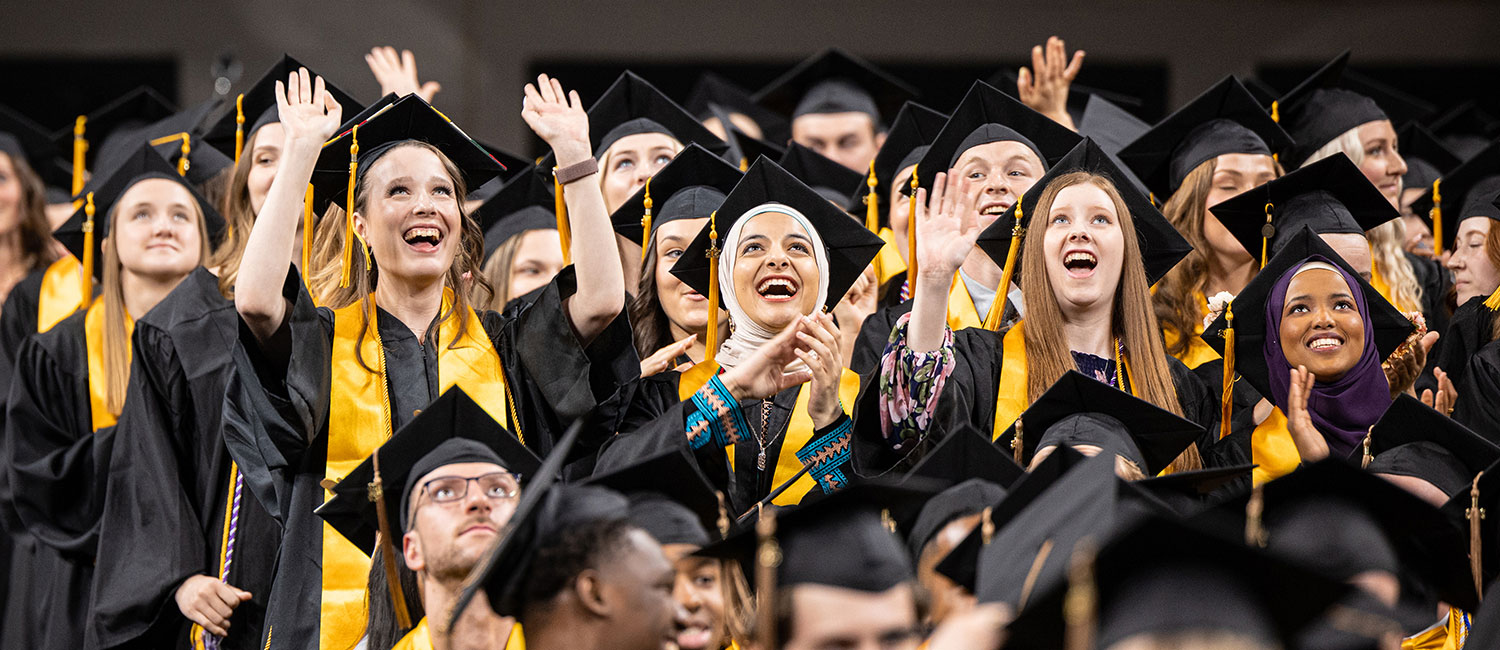 A group of female UWM students wearing graduation robes and cheering