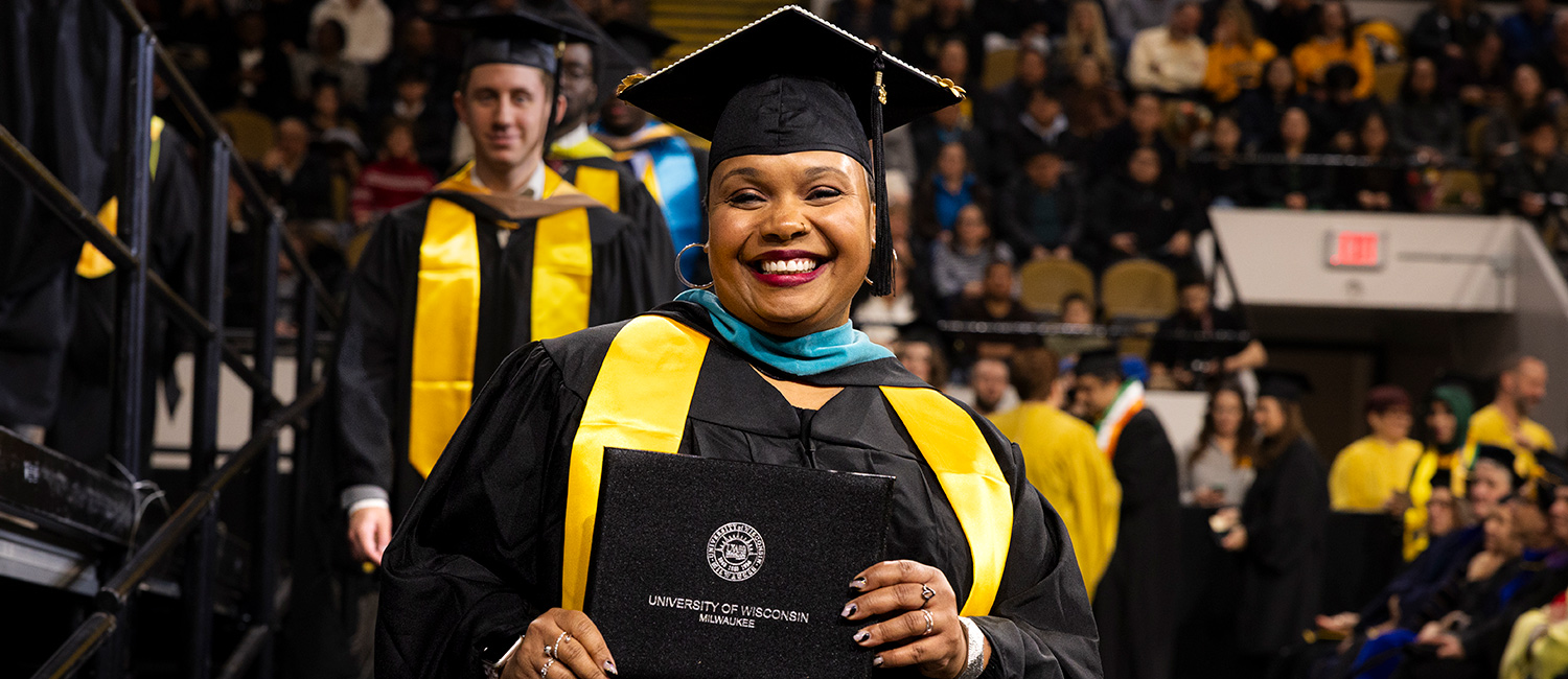 UWM student smiles proudly and holds her diploma at the fall 2025 commencement ceremony