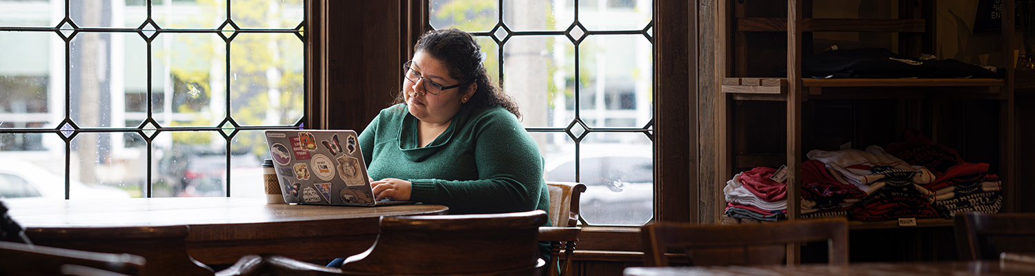 UWM online student working on a laptop at a coffeeshop.