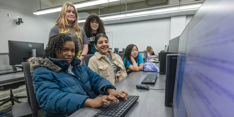 Elementary school students smiling and laughing at a computer at a Girls Who Code youth program.