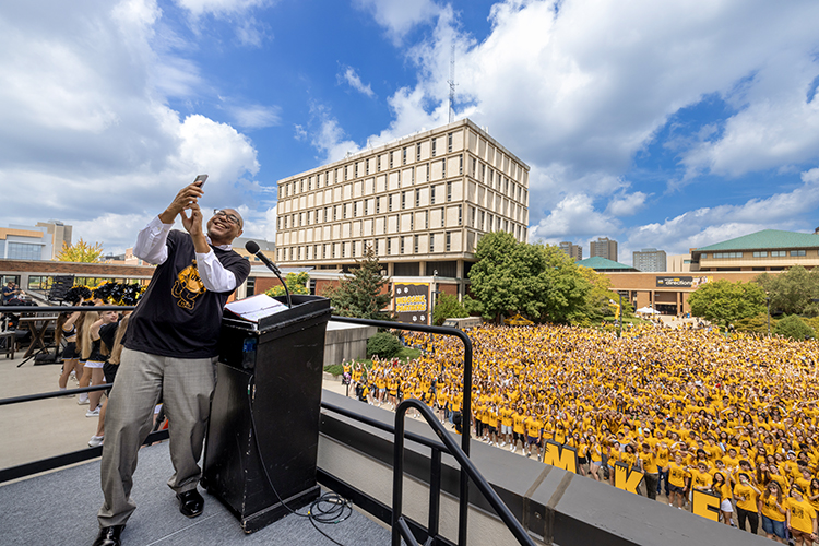 Chancellor Thomas Gibson takes a selfie in front of a large group of people wearing yellow UWM shirts.