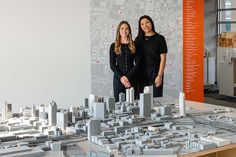 Two women dressed in black stand behind a large 3D model of downtown Milwaukee.