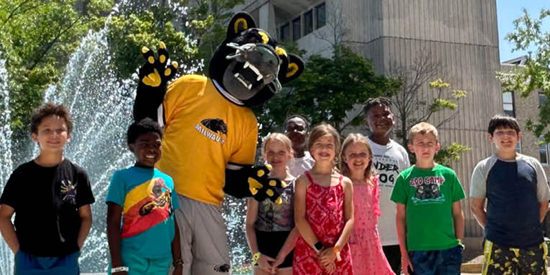 Young students posing for a photo with Pounce in front of the UWM Fountain