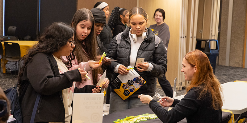 A group of 9th grade students speaking with a woman at a table during a 9th grade tour event